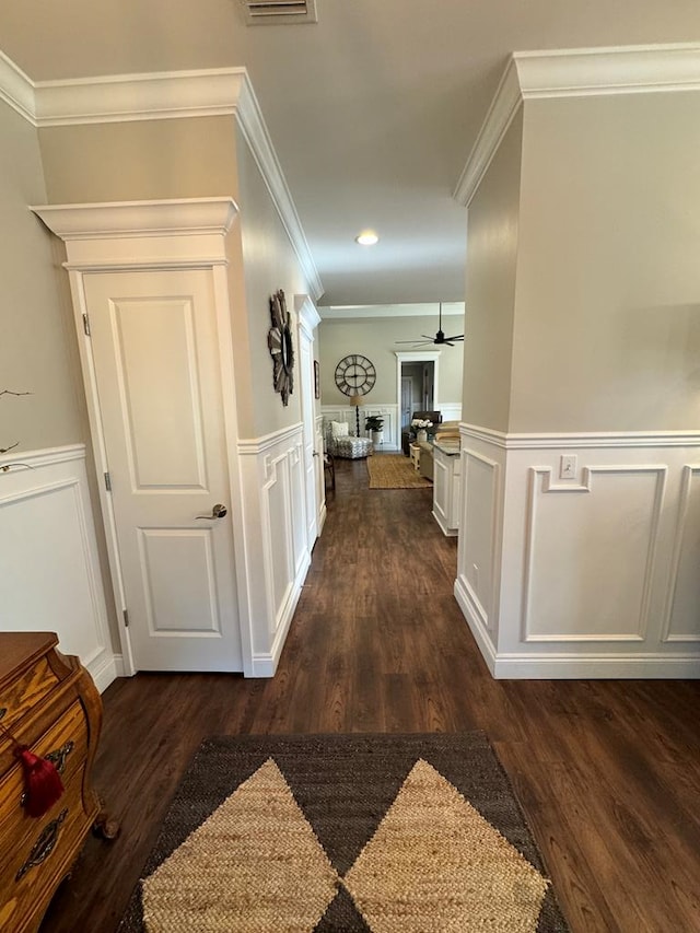 hallway featuring dark wood finished floors, a decorative wall, ornamental molding, and wainscoting