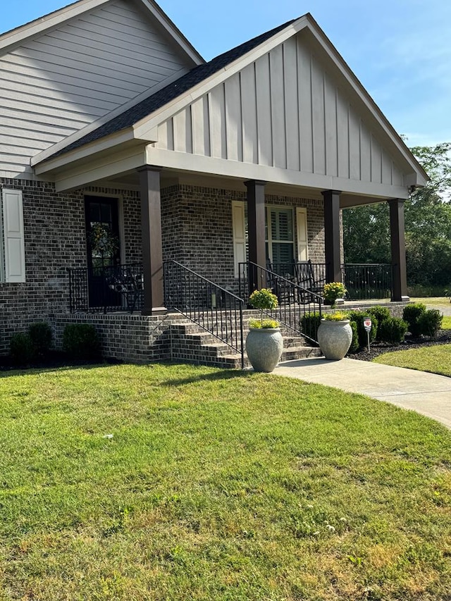 view of front facade with board and batten siding, a front lawn, covered porch, and brick siding