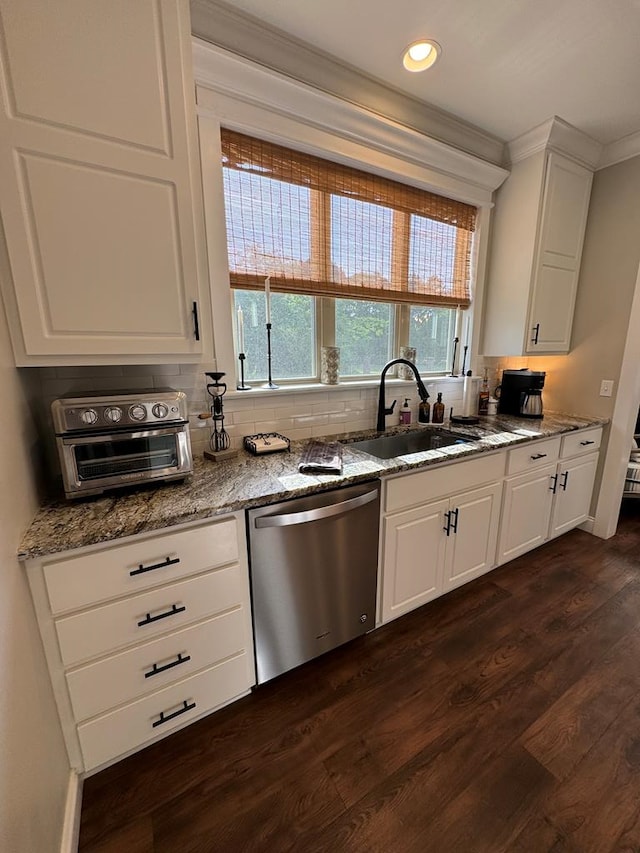 kitchen with dark wood finished floors, stainless steel dishwasher, a sink, light stone countertops, and white cabinetry