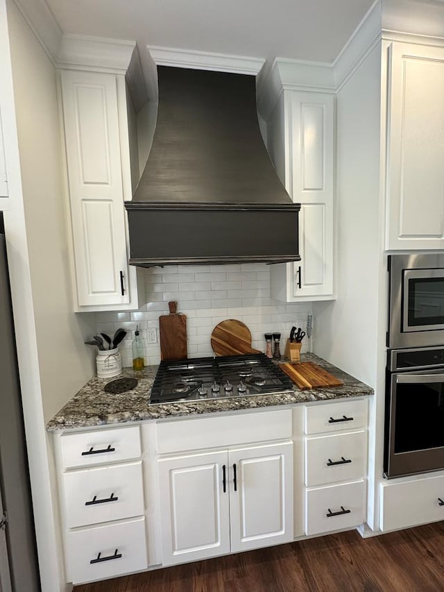 kitchen with stainless steel appliances, dark stone counters, tasteful backsplash, custom exhaust hood, and white cabinetry