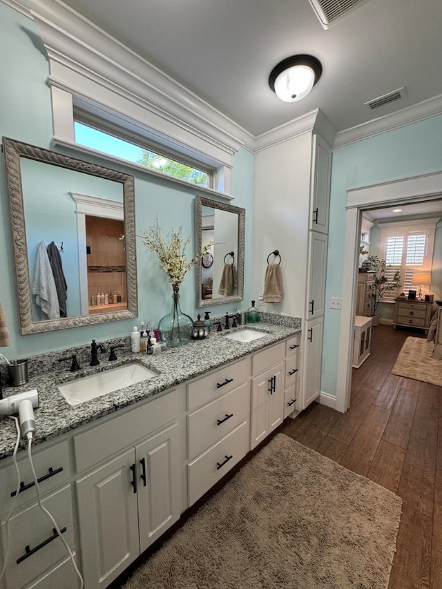bathroom with hardwood / wood-style flooring, crown molding, a sink, and visible vents
