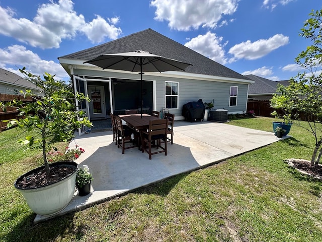back of property with a lawn, a patio area, central air condition unit, fence, and a shingled roof