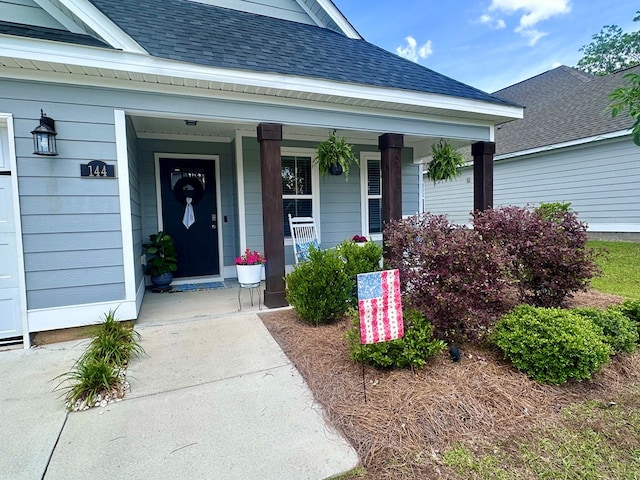 doorway to property with a shingled roof and a porch