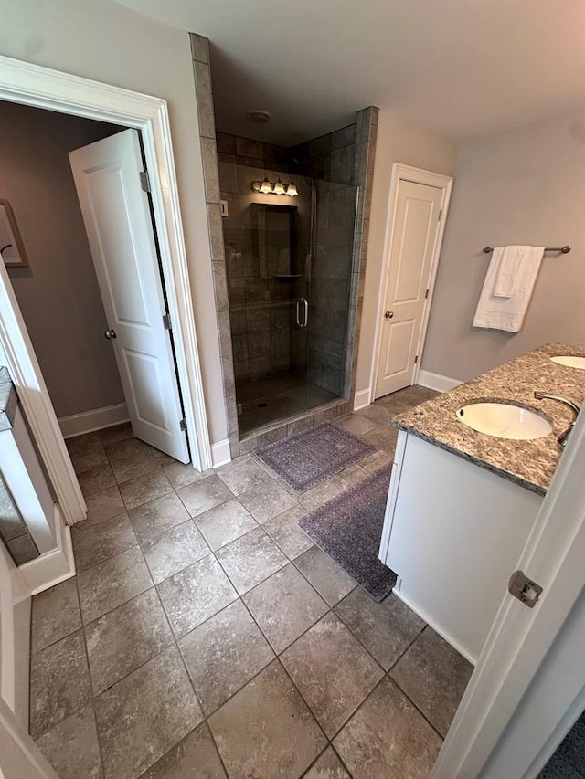 bathroom with double vanity, a stall shower, a sink, baseboards, and stone tile floors