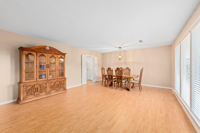 dining area featuring visible vents, light wood-style floors, a textured ceiling, a chandelier, and baseboards