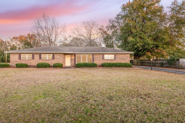 ranch-style home featuring brick siding, fence, and a lawn