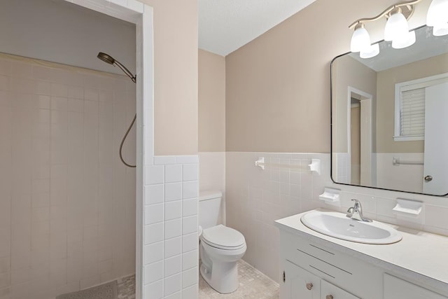 bathroom with tiled shower, toilet, a wainscoted wall, vanity, and tile walls