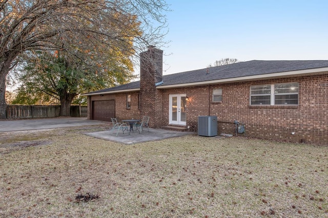 rear view of property with a chimney, an attached garage, fence, a yard, and brick siding