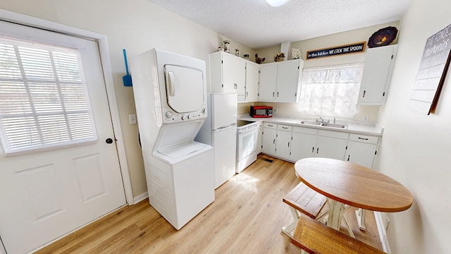 kitchen with sink, white cabinetry, light hardwood / wood-style flooring, white appliances, and stacked washing maching and dryer