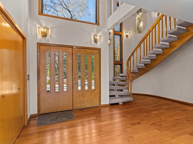 foyer with an inviting chandelier, a towering ceiling, and wood-type flooring