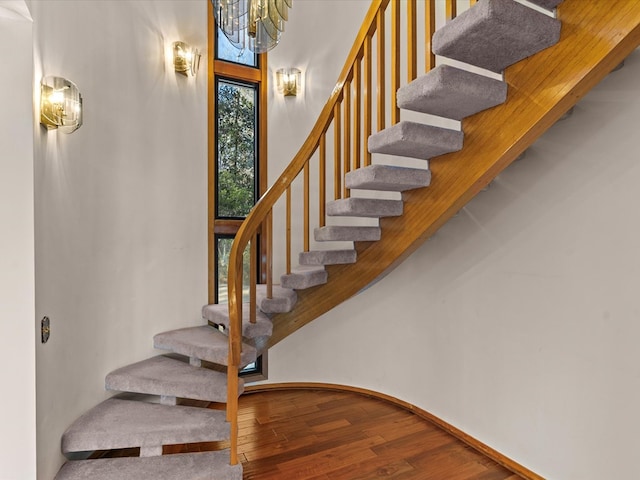 staircase with hardwood / wood-style flooring, a towering ceiling, and a notable chandelier