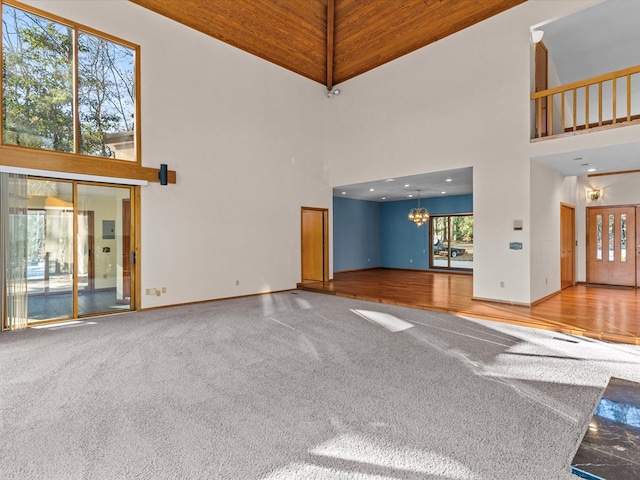 unfurnished living room featuring carpet, wooden ceiling, a notable chandelier, and a towering ceiling