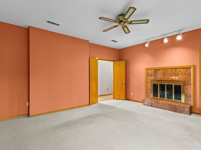 unfurnished living room featuring ceiling fan, carpet, track lighting, and a high end fireplace