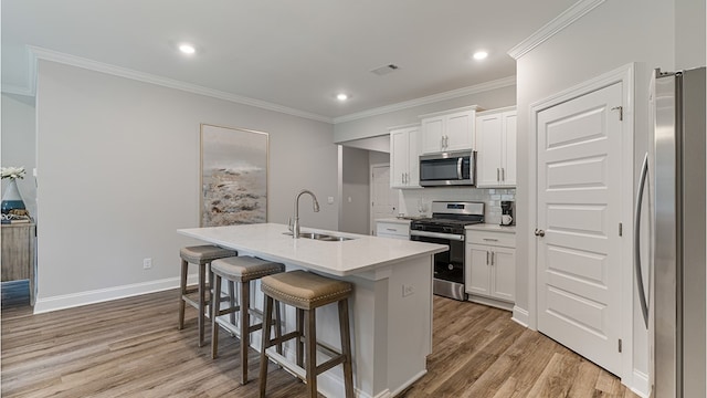 kitchen with a kitchen island with sink, white cabinetry, stainless steel appliances, and a sink