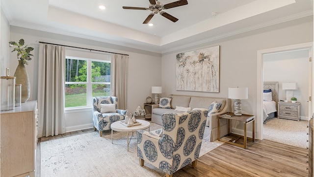 sitting room with baseboards, ceiling fan, ornamental molding, a tray ceiling, and light wood-style floors