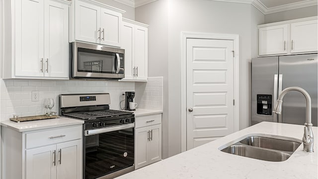 kitchen featuring light stone counters, appliances with stainless steel finishes, ornamental molding, white cabinetry, and a sink