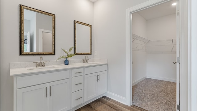 bathroom featuring double vanity, a sink, a walk in closet, and baseboards