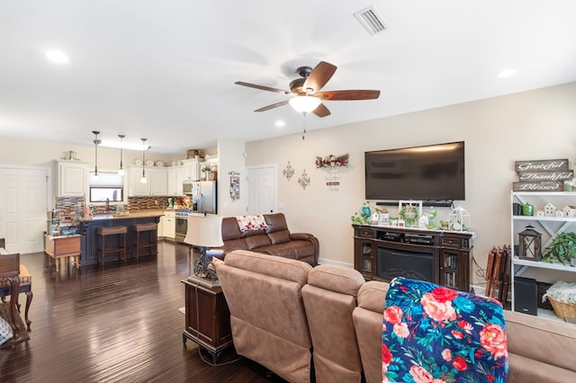 living room with ceiling fan, a fireplace, and dark wood-type flooring