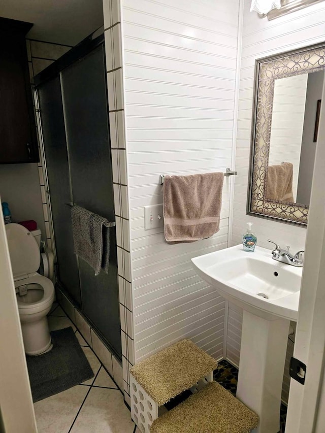 bathroom featuring a shower with door, sink, wooden walls, tile patterned flooring, and toilet