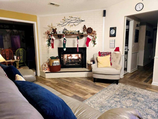 living room featuring a textured ceiling, hardwood / wood-style flooring, a brick fireplace, and ornamental molding