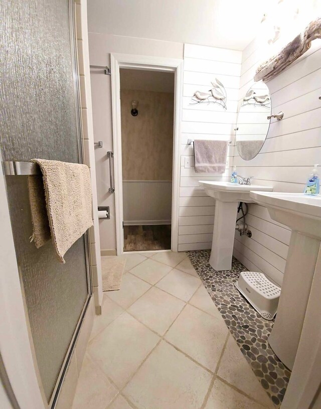 bathroom featuring tile patterned floors, a shower with door, and wood walls