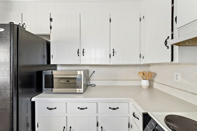 kitchen featuring black refrigerator, stove, and white cabinetry