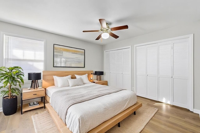 bedroom with light wood-style floors, ceiling fan, and two closets