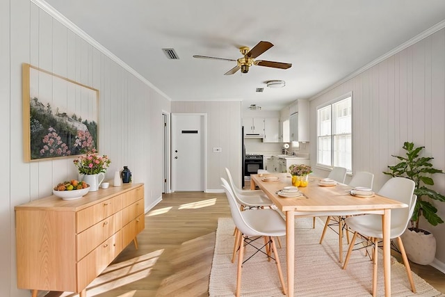 dining space featuring visible vents, baseboards, ceiling fan, ornamental molding, and light wood-type flooring