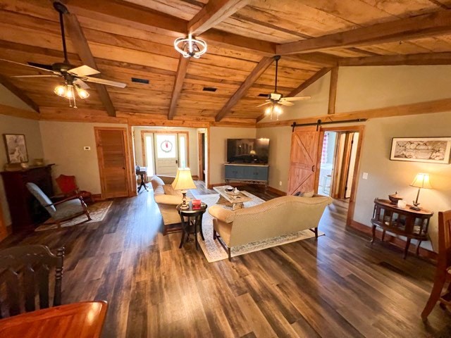 living room featuring dark hardwood / wood-style flooring, ceiling fan, a barn door, lofted ceiling with beams, and wooden ceiling