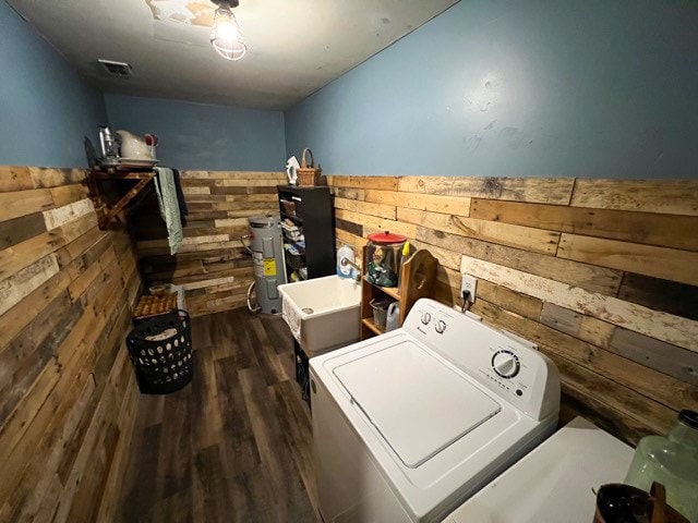 clothes washing area featuring sink, water heater, washer / clothes dryer, dark hardwood / wood-style floors, and wood walls