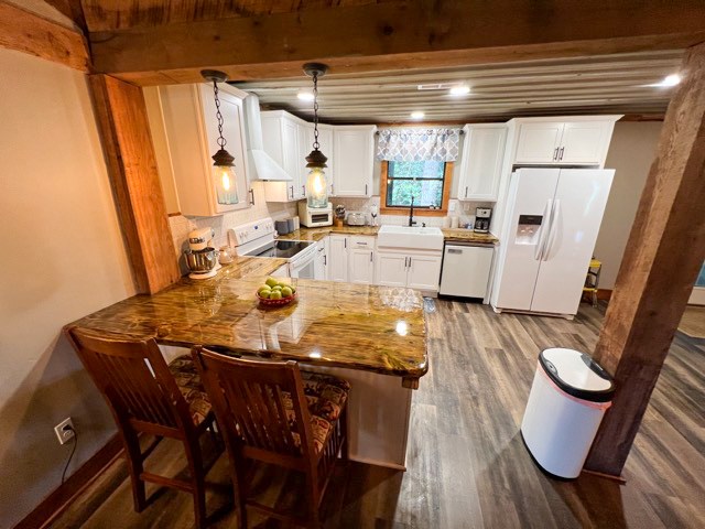 kitchen featuring pendant lighting, white appliances, kitchen peninsula, dark hardwood / wood-style floors, and white cabinetry