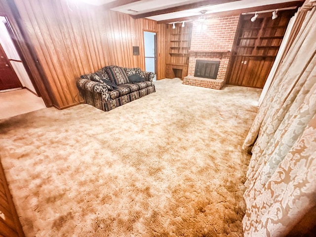 carpeted living room featuring wood walls, a brick fireplace, beam ceiling, and track lighting