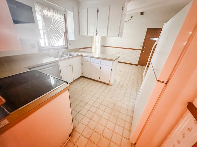 kitchen with wallpapered walls, white cabinets, a peninsula, light countertops, and a sink