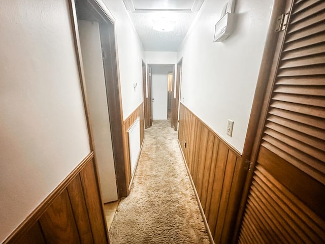 hall featuring light colored carpet, wainscoting, wooden walls, and a textured ceiling