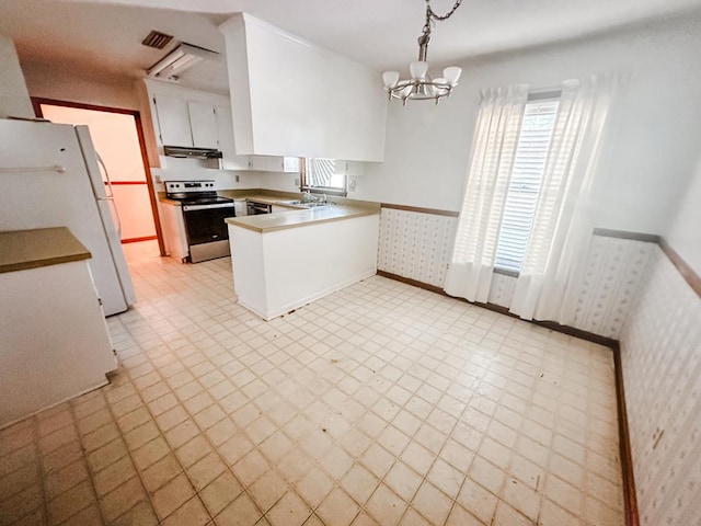 kitchen with wallpapered walls, a wainscoted wall, freestanding refrigerator, a peninsula, and stainless steel range with electric stovetop