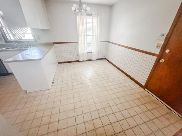 unfurnished dining area featuring a wainscoted wall, a notable chandelier, a wealth of natural light, a sink, and wallpapered walls