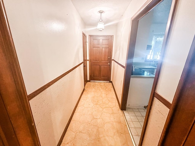 hall featuring a textured wall, stone finish flooring, and baseboards