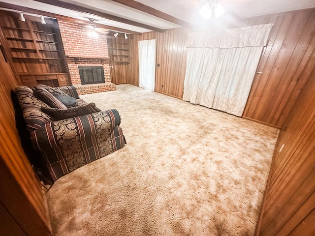 living area with carpet, beam ceiling, a brick fireplace, wood walls, and ceiling fan