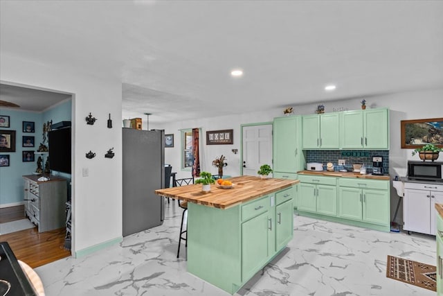 kitchen with black microwave, butcher block countertops, green cabinets, marble finish floor, and freestanding refrigerator