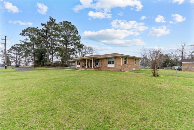 view of front facade with a front yard, covered porch, brick siding, and fence