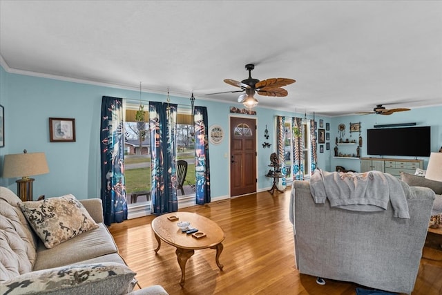 living room with a ceiling fan, crown molding, baseboards, and wood finished floors