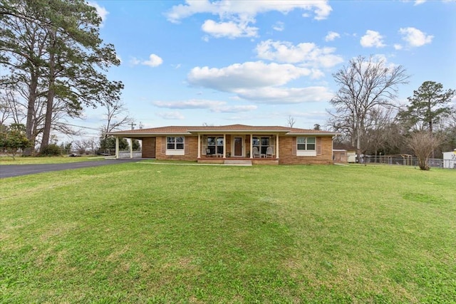 ranch-style home featuring covered porch, fence, driveway, a carport, and a front lawn