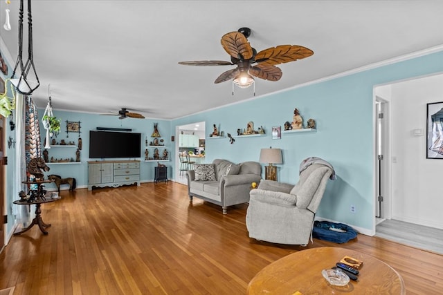 living area featuring crown molding, baseboards, ceiling fan, and wood finished floors