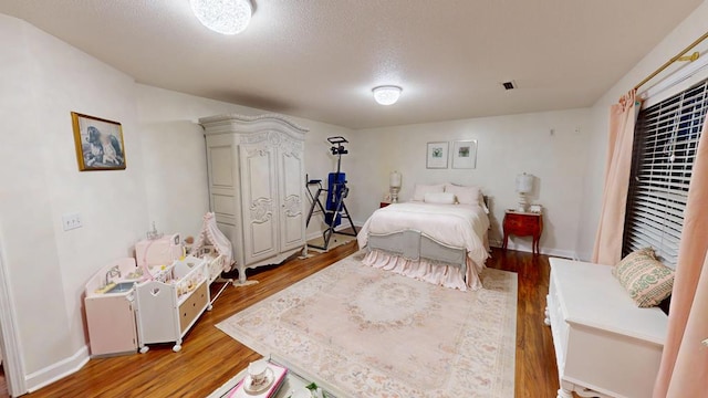 bedroom with a textured ceiling, baseboards, and light wood-style floors