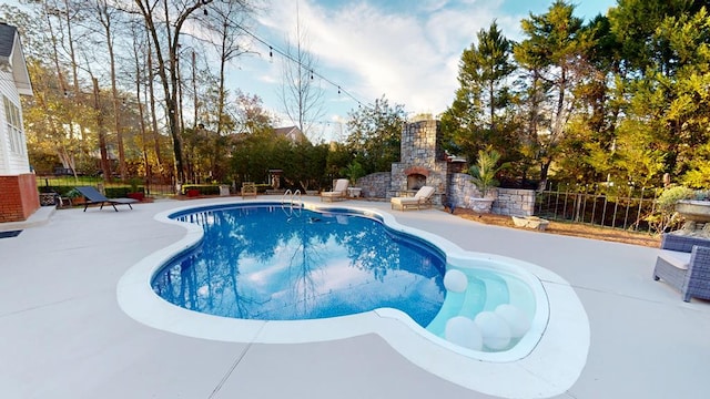 view of swimming pool with a patio, fence, and an outdoor stone fireplace