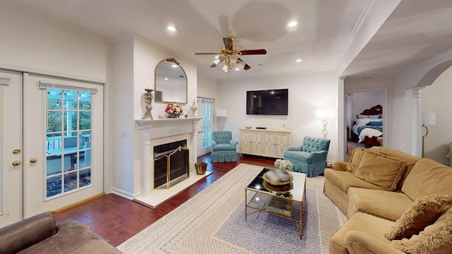 living area featuring a fireplace, wood finished floors, arched walkways, and ornamental molding