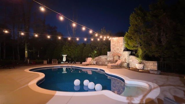 pool at night featuring a patio, a fireplace, and a fenced in pool