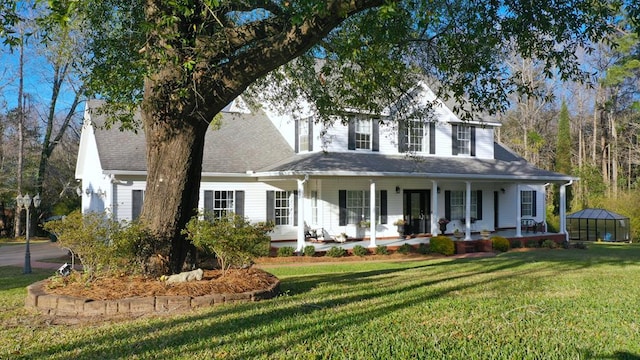 view of front facade with roof with shingles, covered porch, and a front yard