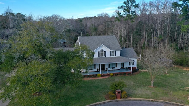 view of front of house with covered porch, a view of trees, and a front lawn