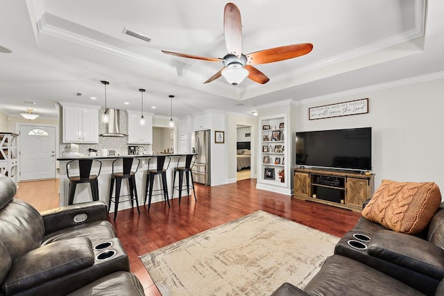 living room with dark hardwood / wood-style flooring, ceiling fan, a raised ceiling, and ornamental molding